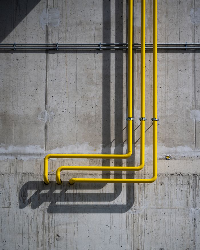 Services Vertical yellow pipes casting shadows on a rugged concrete wall in Berlin.