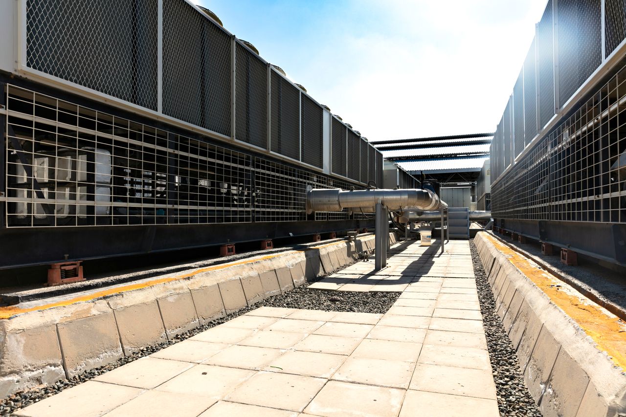 Mastering the First Impression: Your intriguing post title goes here View of a large industrial cooling system with metal pipes and grids outdoors under bright daylight.
